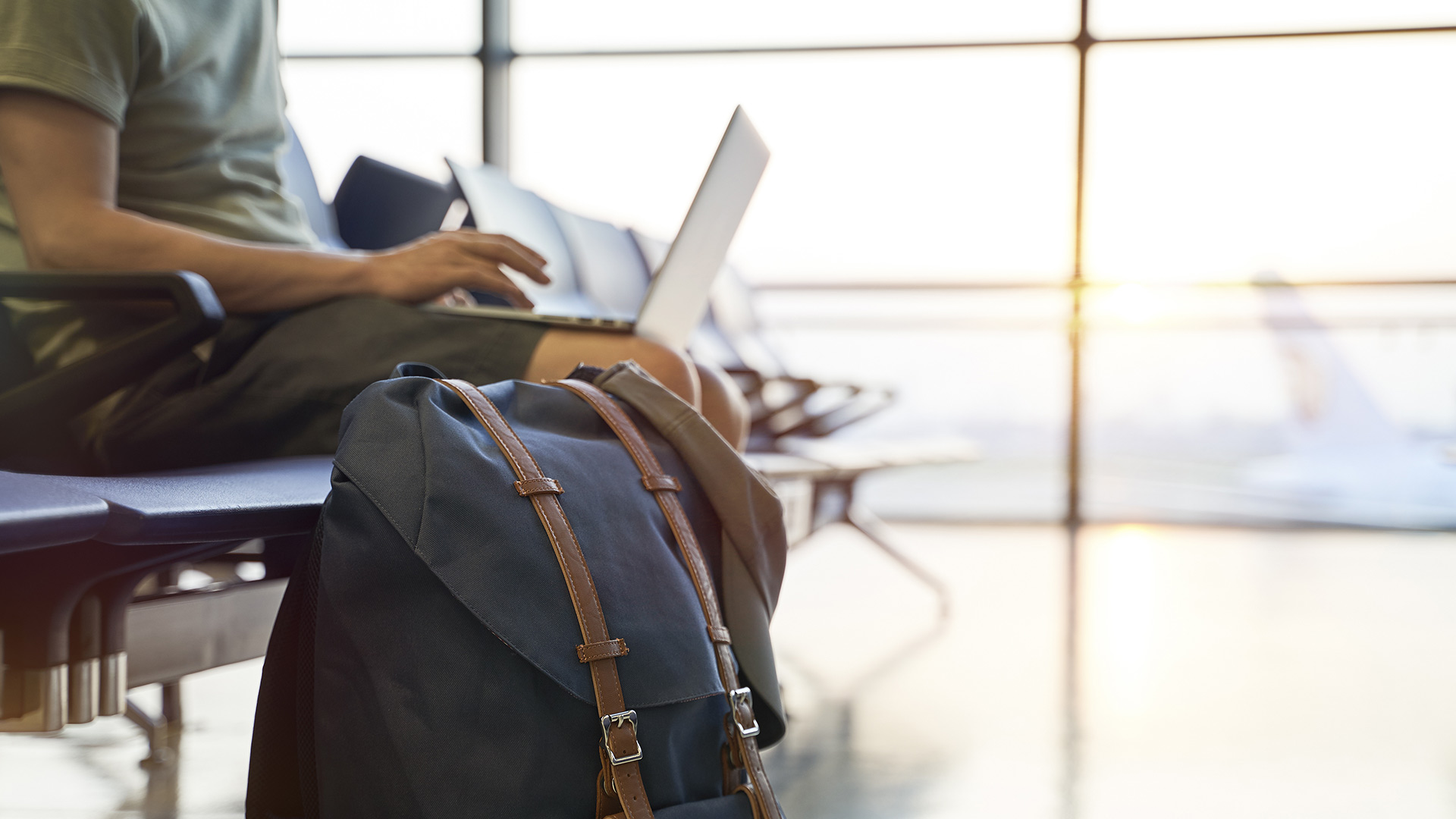 A man on a laptop, seated in an airport with luggage