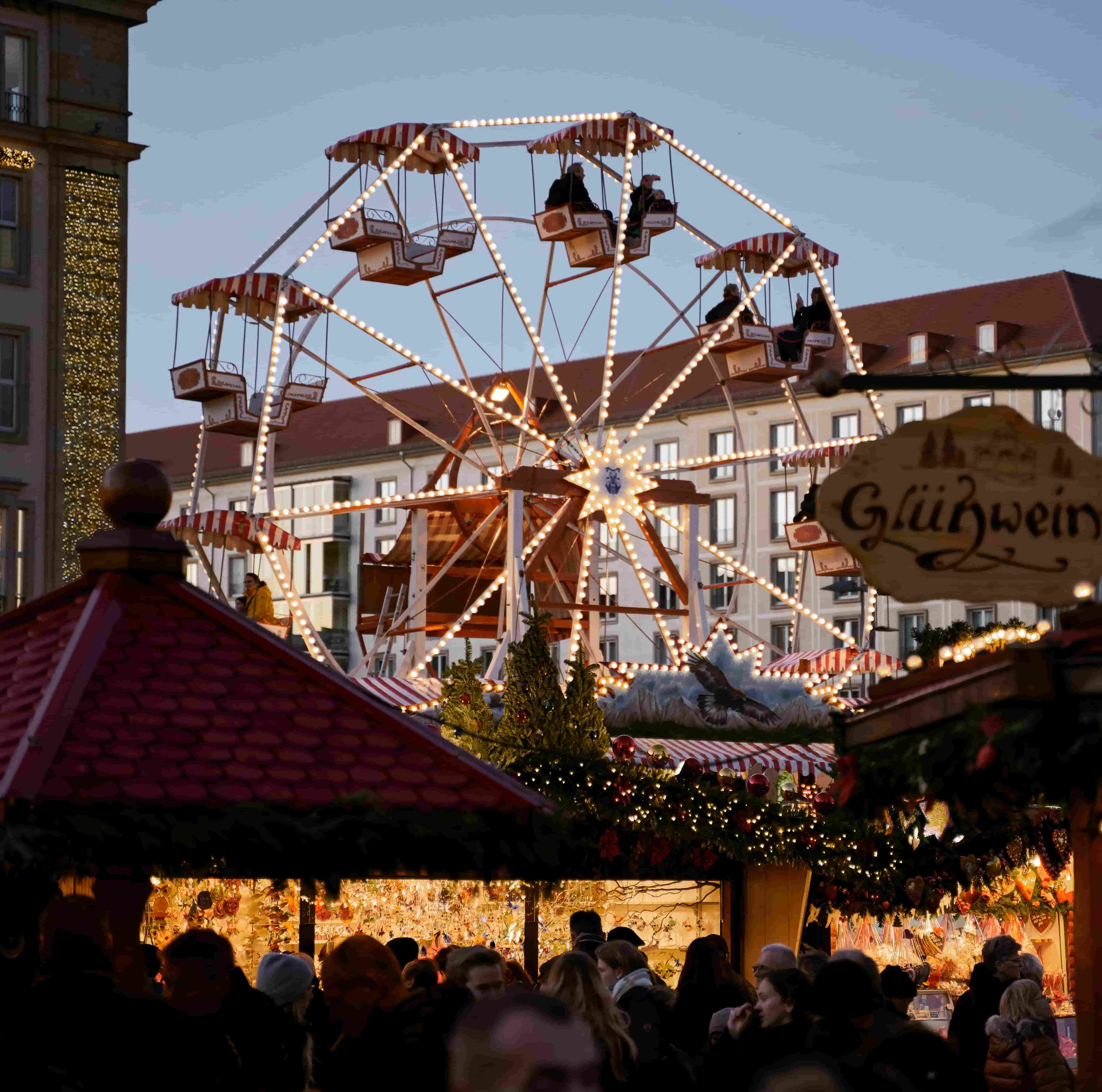 a ferris wheel sits in focus among the warm chaos of the bustling christmas market