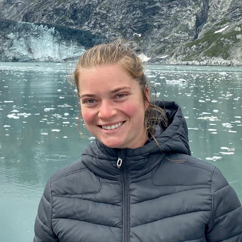 Isabel Johnson Isabel is smiling at the camera in front of a body of water with pieces of ice floating haphazardly.