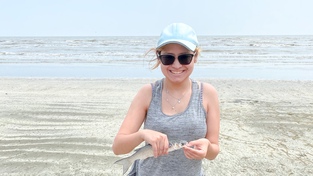 Victoria Ontiveros Victoria is on the beach holding a fish with both hands.