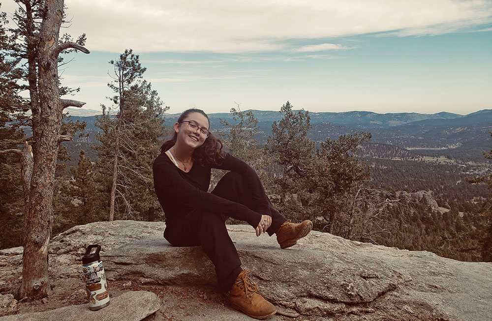 Quinn Shefman An individual sits on a rock on an overlook with forested rolling hills in the background.