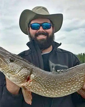 Richard Dotter Richard is holding a large fish. He is wearing a hat and sunglasses and smiling at the camera.