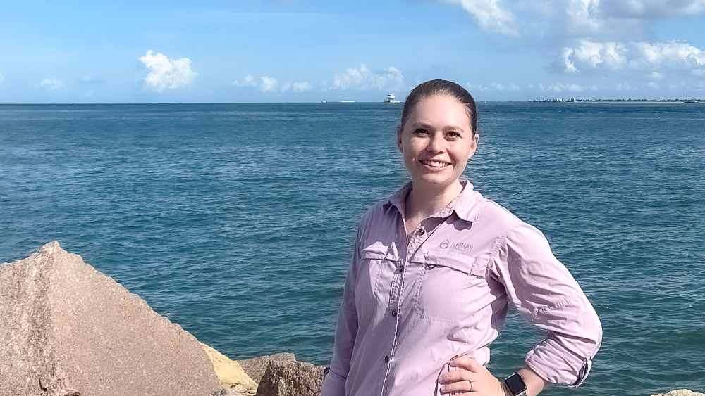 Melanie Rogers An individual standing on rocky shore with the ocean and a clear sky in the background.