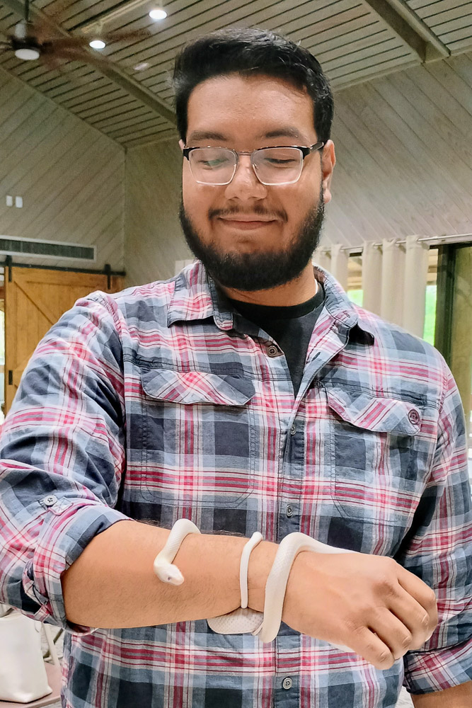 Person in a red and gray plaid shirt holding a small white snake wrapped around their forearm indoors.