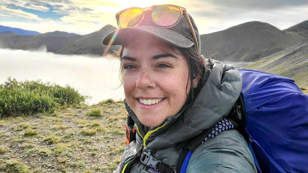 Bailey Steward A person in outdoor gear stands in front of a scenic backdrop of mist-covered mountains.