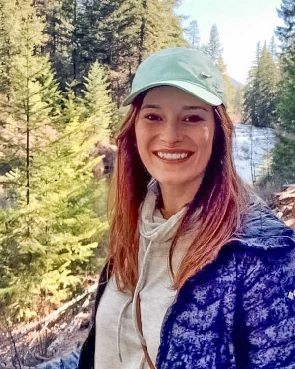 Rachel Sanchez Rachel is outside with evergreen trees in the backround.