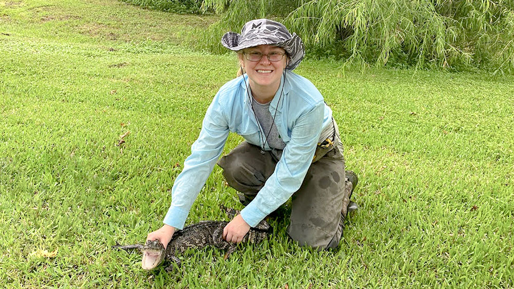 Taylor Thomisee Taylor is kneeling on one knee while holding down a small alligator.