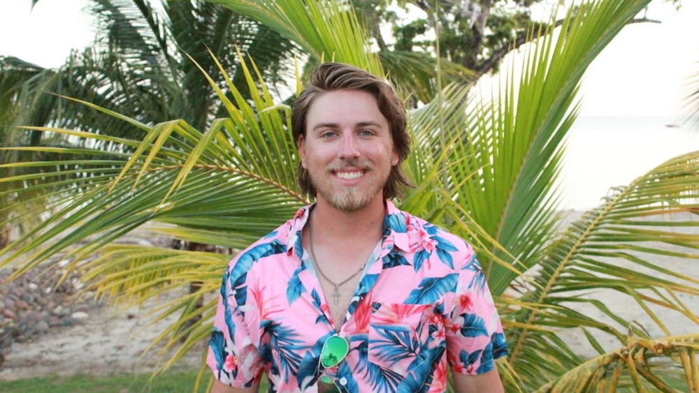 Joshua Ward Joshua is standing in front of a palm tree on beach. He is wearing a colorful Hawaiian shirt and smiling at the camera.