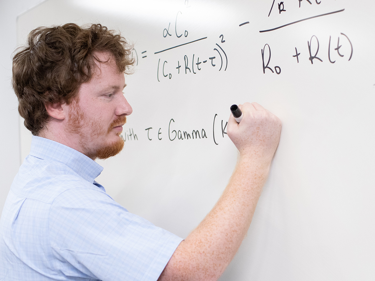 Photo of a math program student writing an equation on a white board